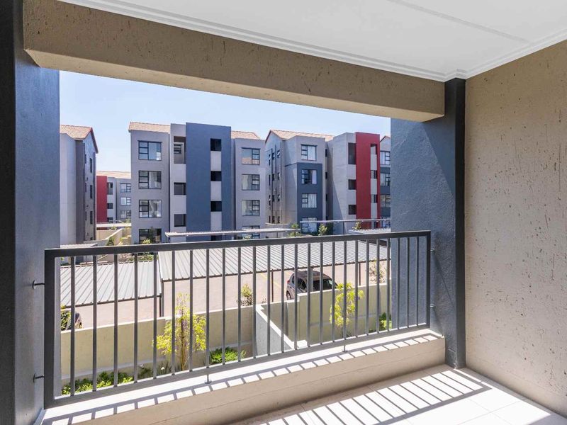 A clean, covered balcony featuring a metal balustrade and tiled flooring, offering an open view of the surrounding apartment complex.