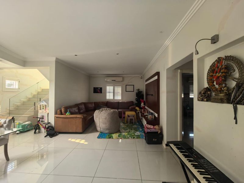 Spacious living area featuring tiled flooring, a glass balustrade staircase, and a built-in wall niche, offering a bright and open layout.
