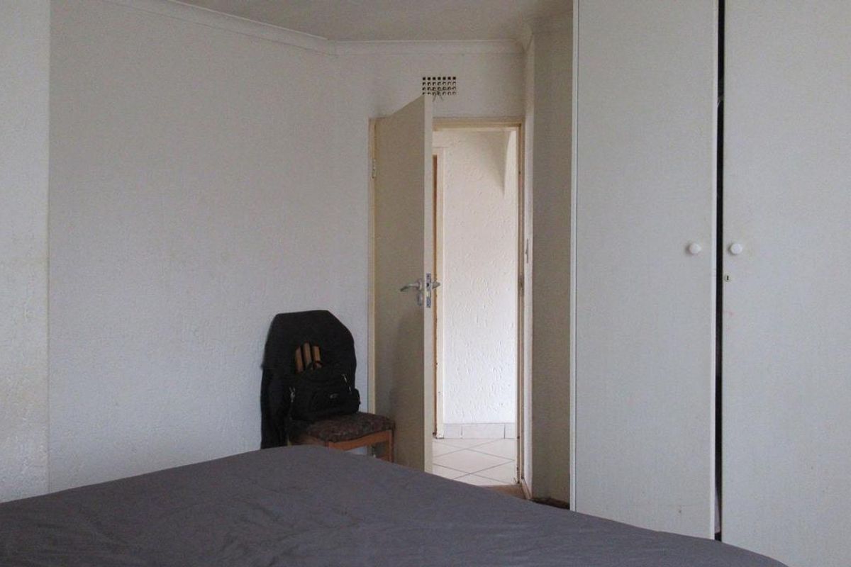 A bedroom featuring built-in cupboards and a doorway leading to an adjacent tiled area.