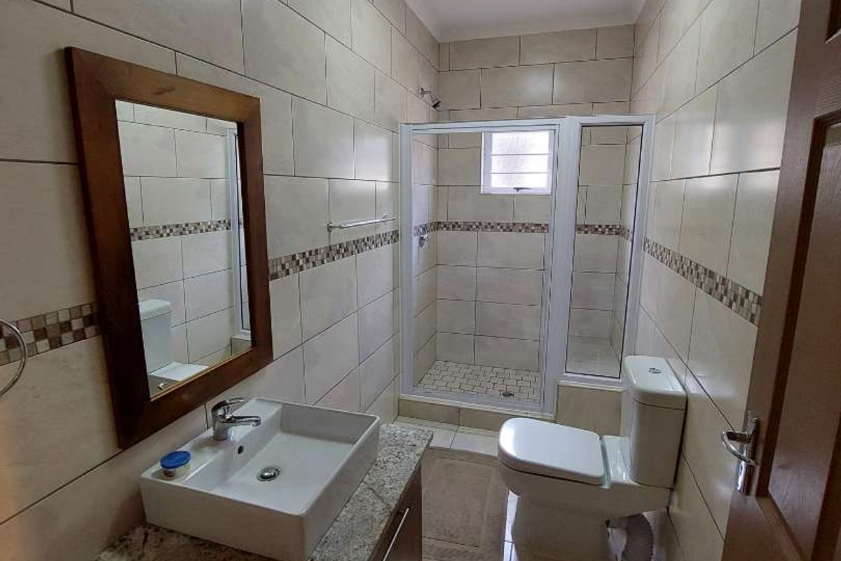 A well-maintained bathroom featuring a granite-topped vanity, vessel sink, tiled walls, and a glass-enclosed shower unit.