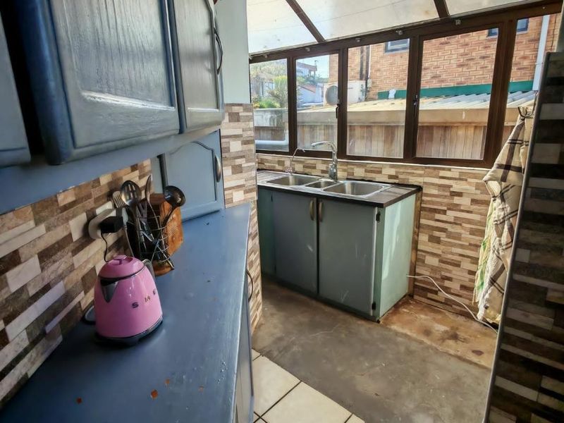 A functional scullery area featuring built-in cabinetry, a double sink, and a tiled backsplash, illuminated by a translucent roof structure.