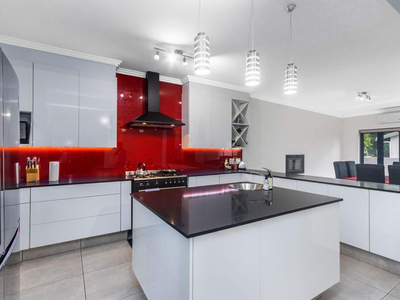 Modern open-plan kitchen featuring a central island, high-gloss cabinetry, striking red glass splashback, and integrated appliances, flowing into a spacious living and dining area.