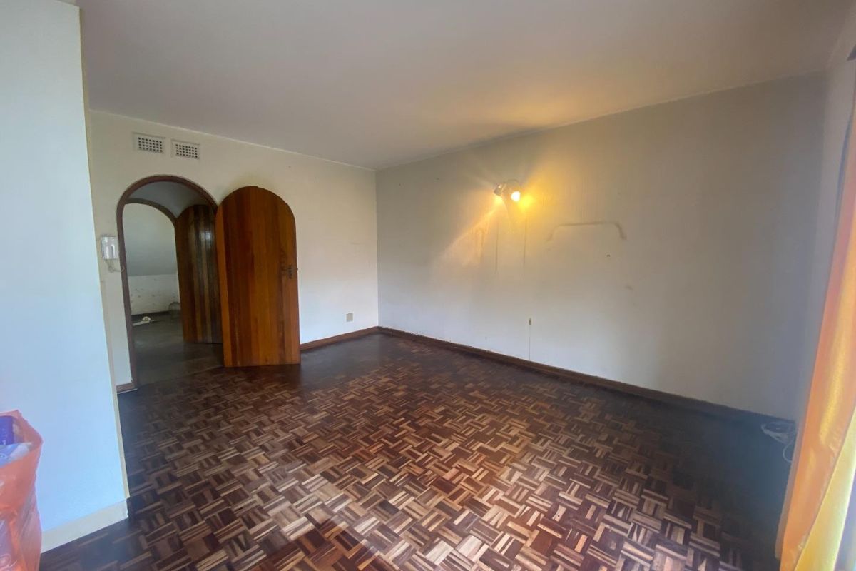 An empty bedroom featuring original parquet flooring and an arched wooden doorway, requiring minor cosmetic updates to the wall finishes.
