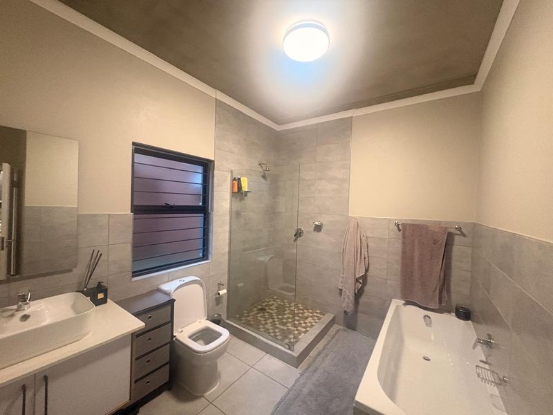 Modern bathroom featuring a vanity with vessel sink, separate glass-enclosed shower, and a bathtub with neutral wall tiling.