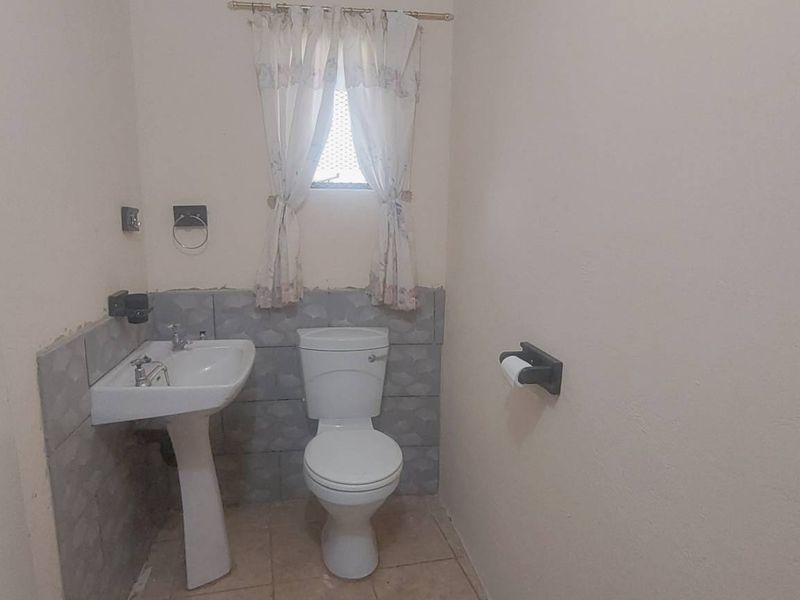 A compact bathroom featuring a pedestal washbasin and toilet with partial wall tiling and tiled flooring.