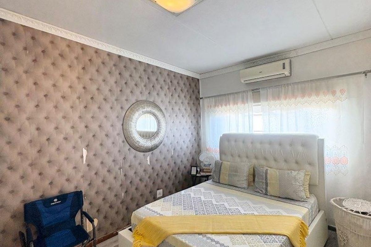 A bedroom featuring a tufted accent wall, wood-look laminate flooring, and a wall-mounted air conditioning unit.