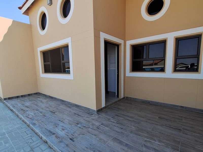 A clean, modern covered patio area featuring wood-look floor tiles, distinctive porthole windows, and well-maintained exterior wall finishes.