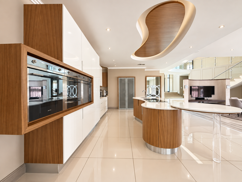 Modern luxury kitchen featuring high-gloss cabinetry, integrated appliances, a curved wooden island with stone countertop, and a unique architectural ceiling feature.