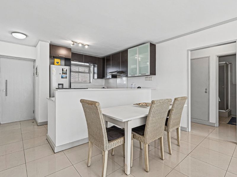 Open-plan kitchen and dining area featuring dark cabinetry, a breakfast bar, and neutral tiled flooring throughout.