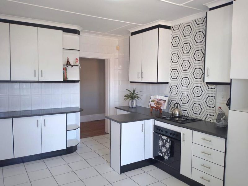 A functional kitchen featuring white cabinetry with black trim, dark countertops, a patterned tiled backsplash, and ceramic floor tiles.