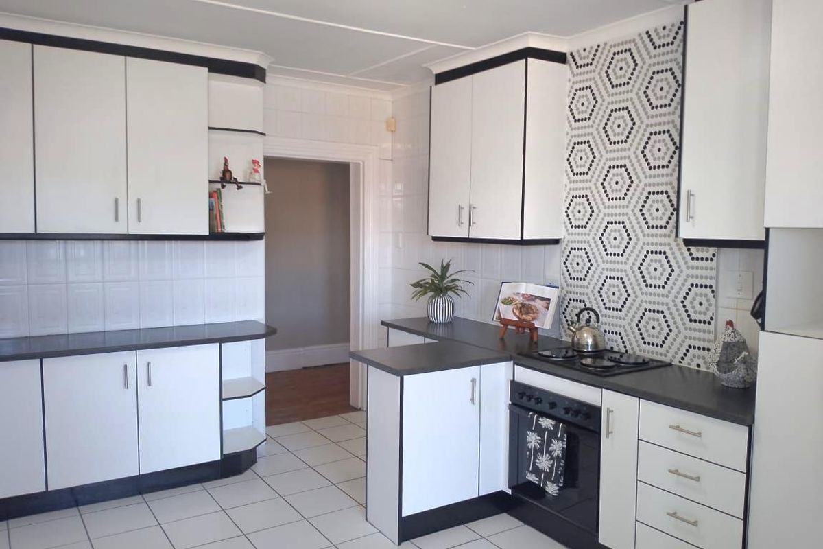 A functional kitchen featuring white cabinetry with black trim, dark countertops, a patterned tiled backsplash, and ceramic floor tiles.