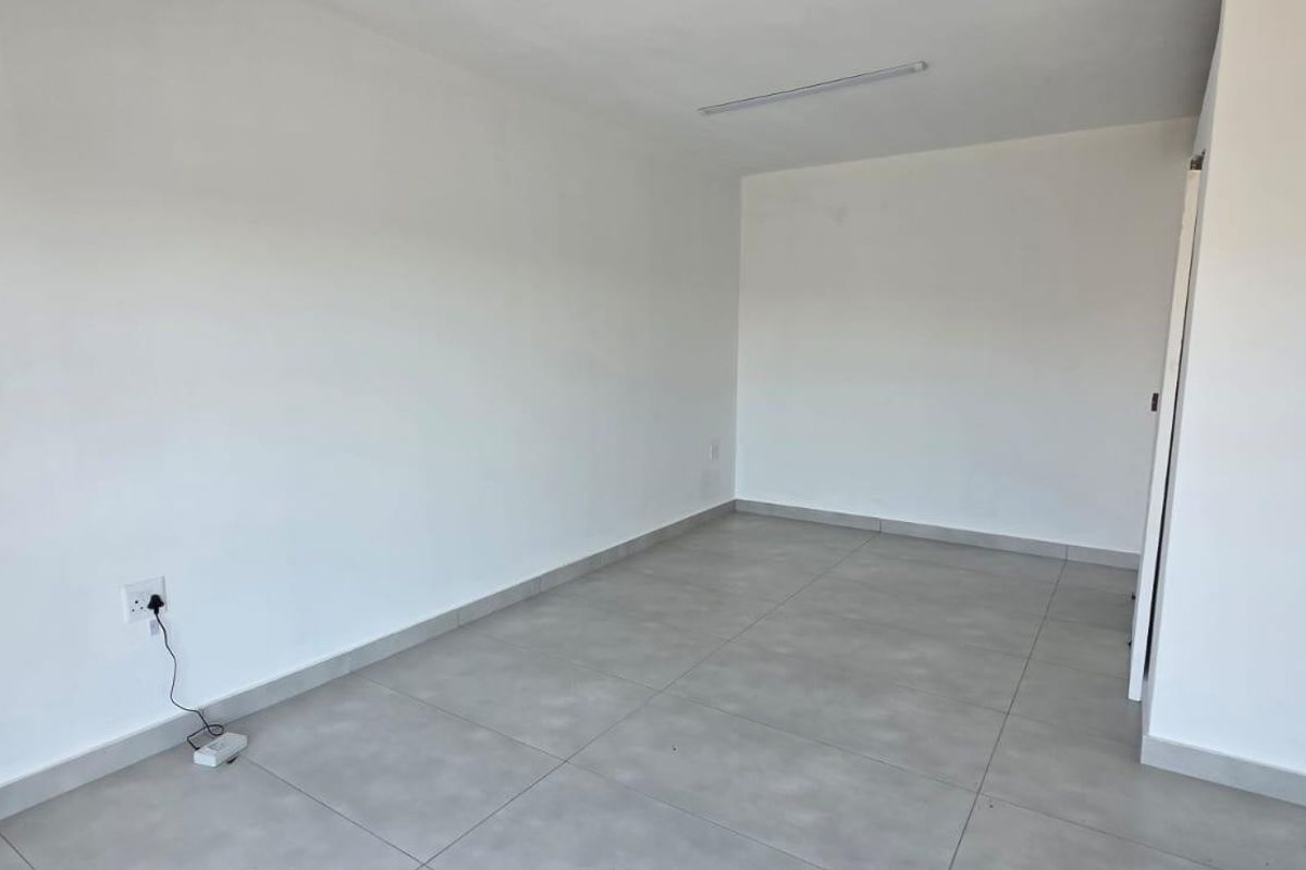 A clean, empty interior space featuring neutral grey floor tiles, white walls, and a functional overhead light fixture, ready for custom fit-out.