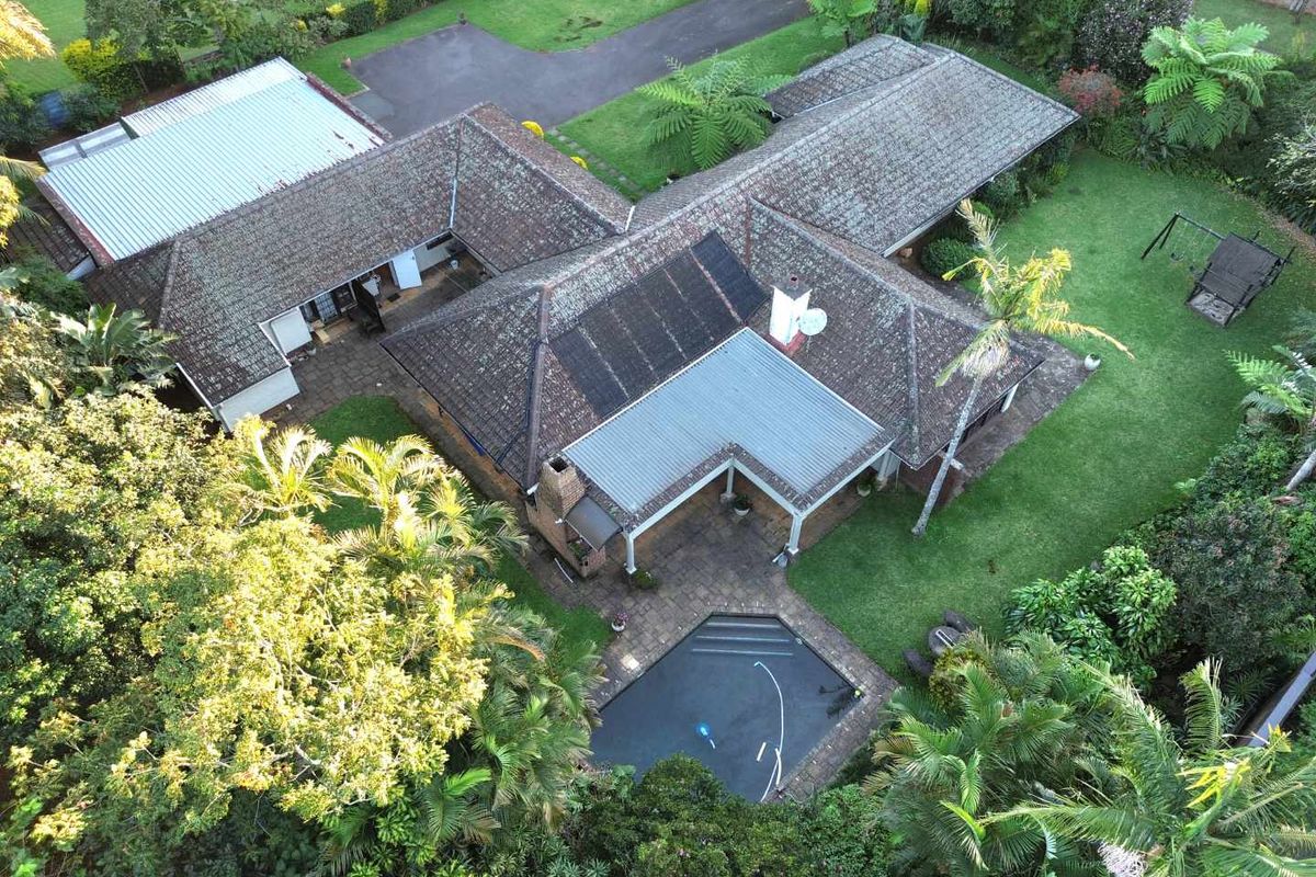 Aerial view of a residential property featuring a swimming pool, expansive garden, paved patio area, and a multi-section tiled roof with solar panels.