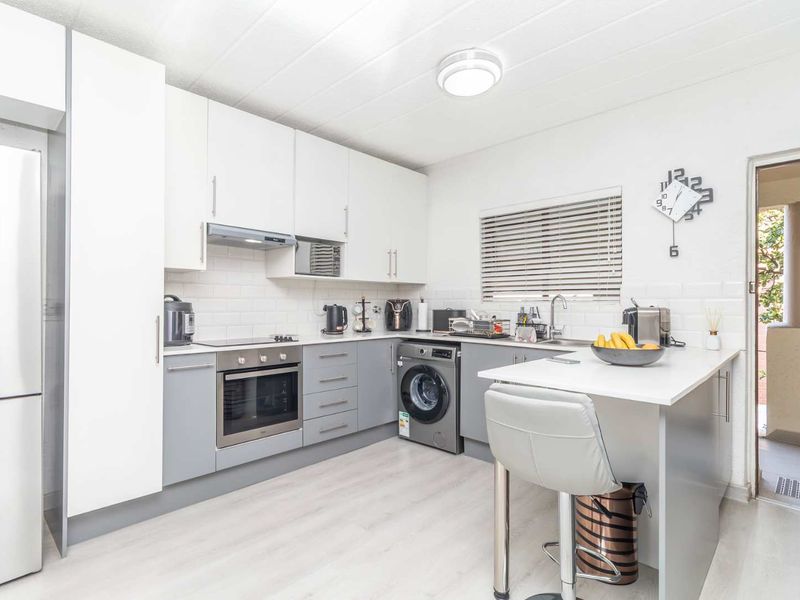 Modern kitchen featuring white and grey cabinetry, subway tile backsplash, built-in oven, extractor fan, integrated washing machine, and a functional breakfast bar.