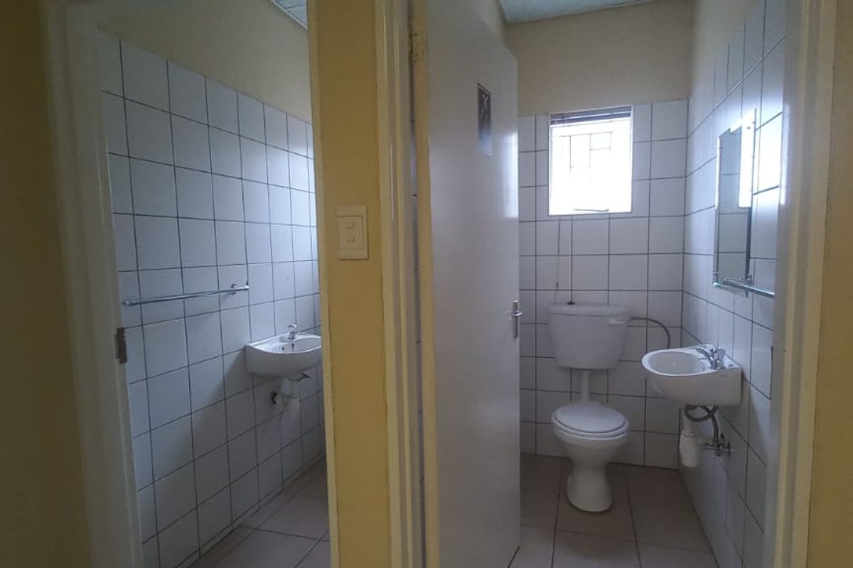 A functional bathroom facility featuring tiled walls, a standard toilet, and a wall-mounted basin, providing essential amenities for a mixed-use property.