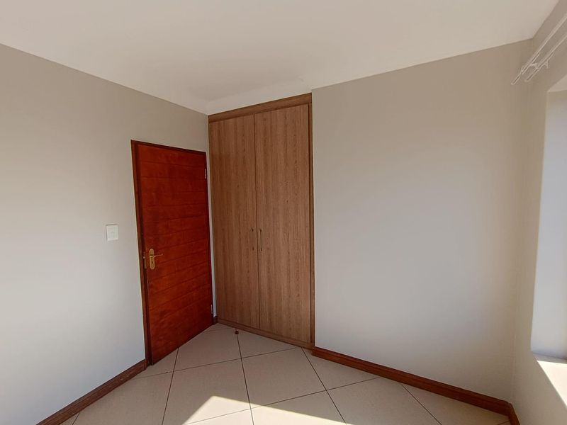 A clean, empty bedroom featuring neutral wall paint, tiled flooring, and a built-in wooden wardrobe.