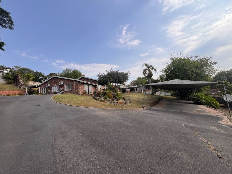 Front view of a face brick house featuring a large asphalt driveway, a carport, and established garden landscaping.