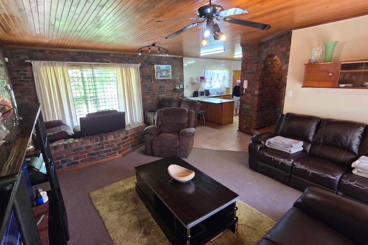 Open plan living area featuring exposed brick walls, timber ceiling, and a connected kitchen space with a central island.