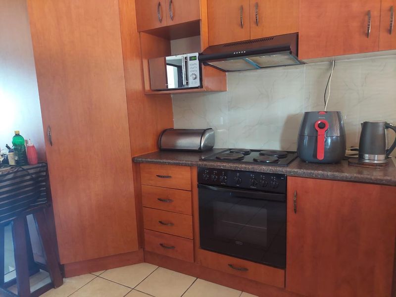 A functional kitchen featuring wood-finish cabinetry, laminate countertops, a built-in oven with electric hob, and tiled flooring.