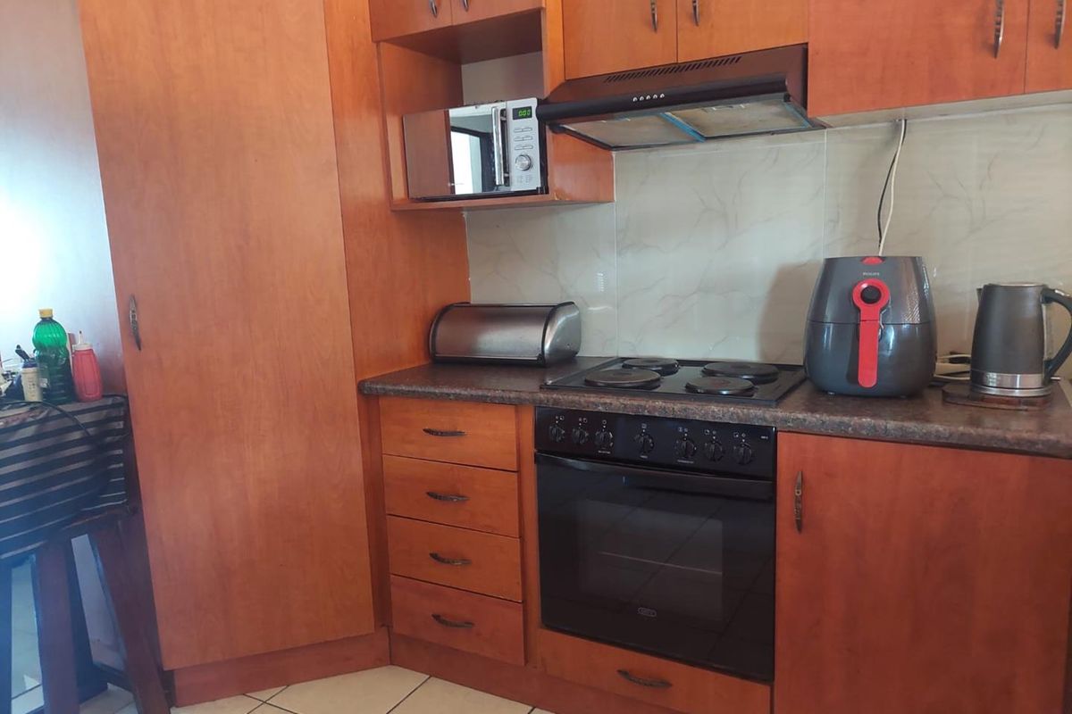 A functional kitchen featuring wood-finish cabinetry, laminate countertops, a built-in oven with electric hob, and tiled flooring.