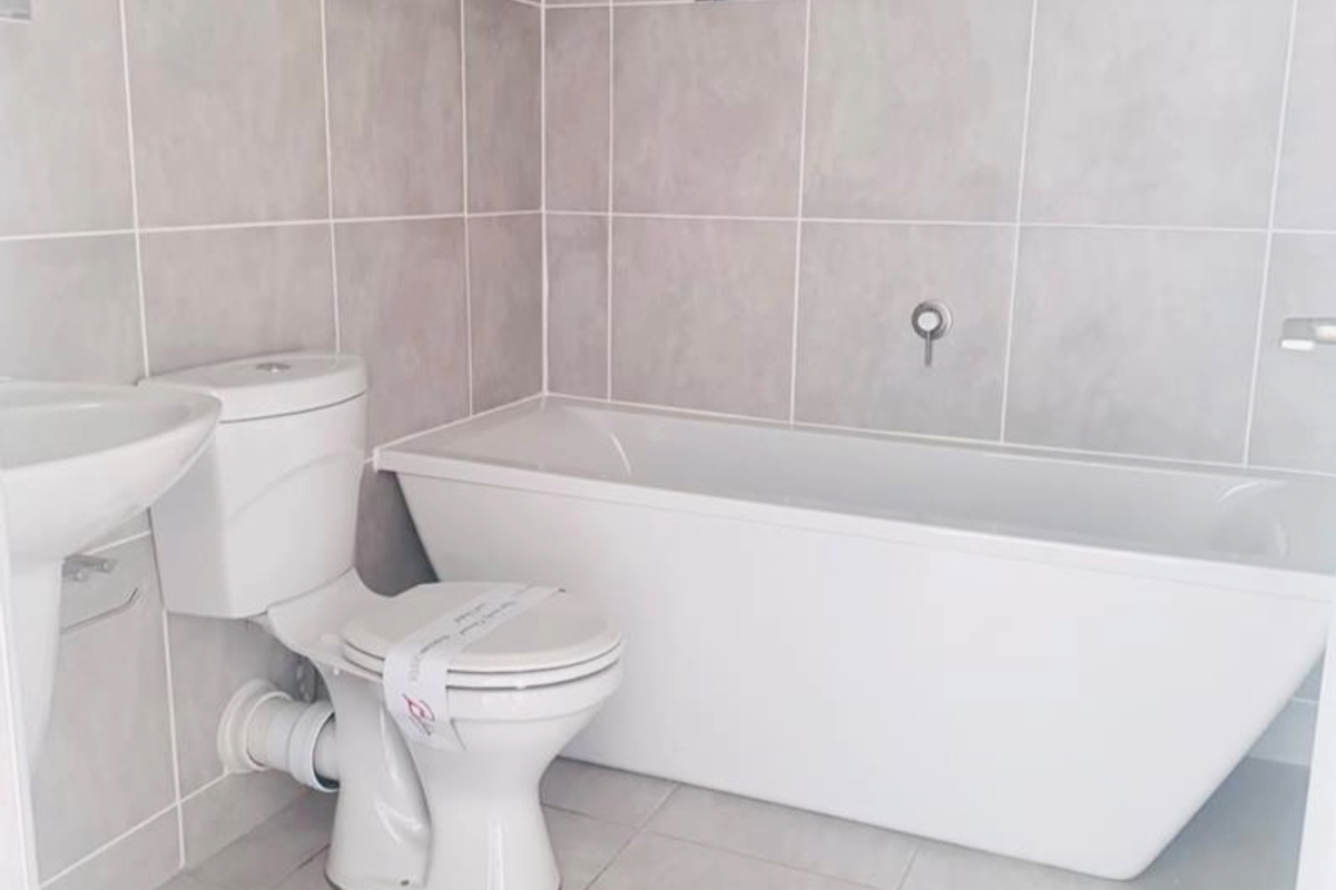 A modern, clean bathroom featuring a white freestanding bathtub, pedestal sink, and ceramic toilet with neutral wall and floor tiling.