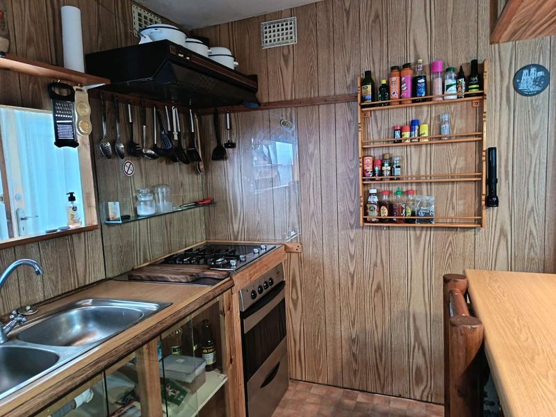 A compact kitchen featuring wood paneling, a built-in oven, gas cooktop, and stainless steel sink, reflecting a dated aesthetic in need of modernization.