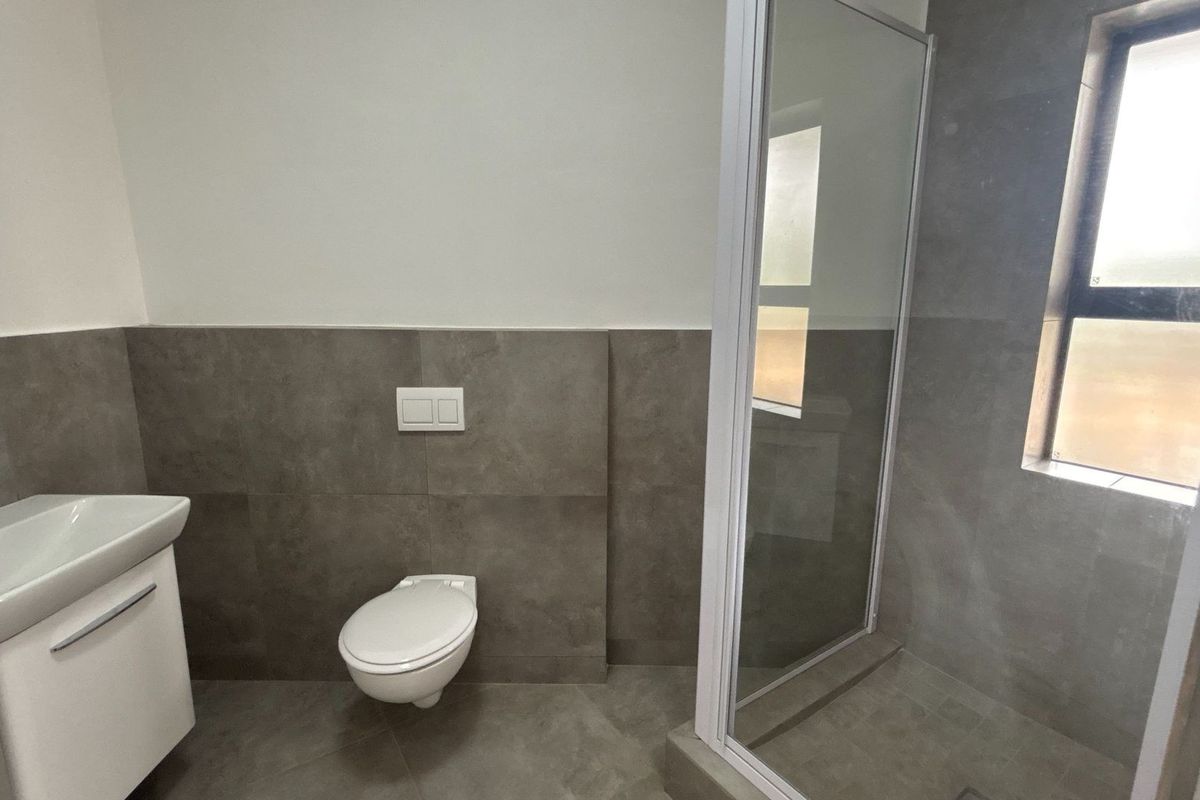 Modern bathroom featuring a wall-hung toilet, vanity basin, and a glass-enclosed shower with grey floor-to-ceiling tiling.