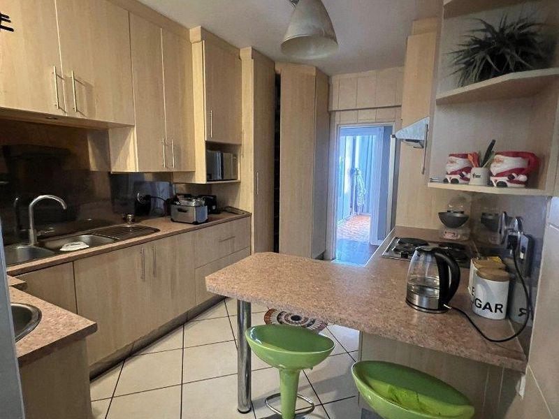 A functional kitchen featuring light wood-tone cabinetry, laminate countertops, a breakfast bar, and tiled flooring, with direct access to an outdoor area.