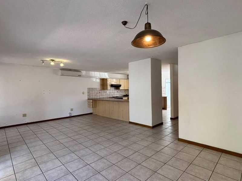 Spacious open-plan living and kitchen area featuring neutral tiled flooring, built-in cabinetry, and a split-system air conditioner.