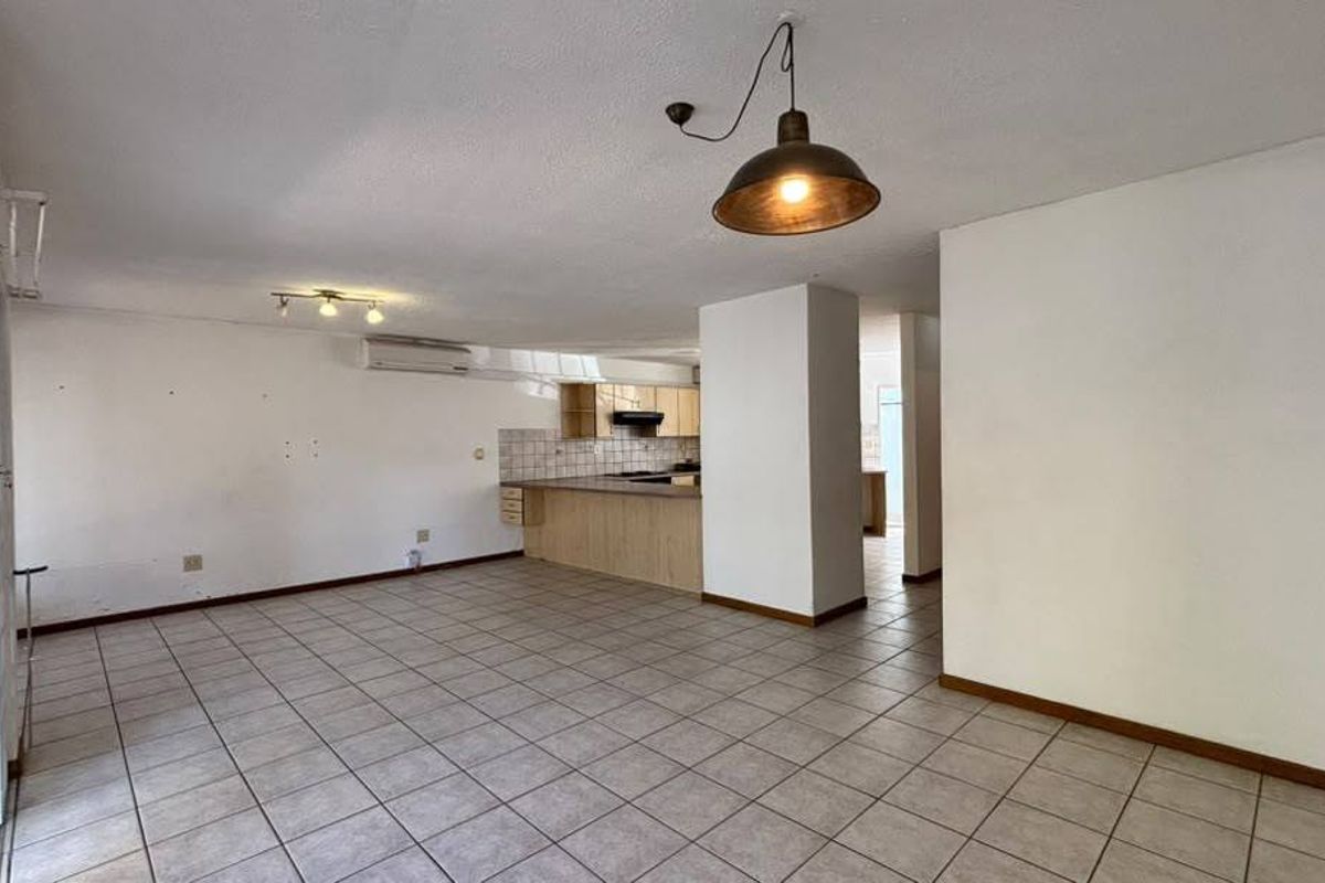 Spacious open-plan living and kitchen area featuring neutral tiled flooring, built-in cabinetry, and a split-system air conditioner.