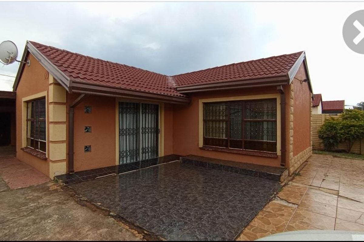 Exterior view of a single-story house featuring a tiled patio, sliding glass doors with security gates, and a pitched roof.