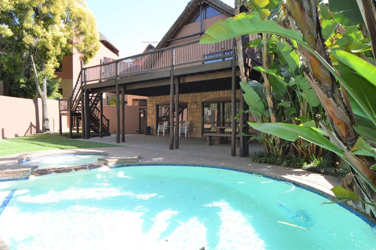 Rear exterior view featuring a swimming pool, paved patio area, and a raised timber deck attached to the main building structure.