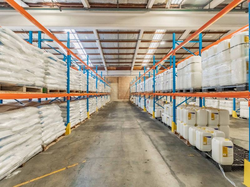 Industrial warehouse space featuring high-capacity steel racking systems, durable concrete flooring, and exposed roof trusses with integrated skylights for natural illumination.