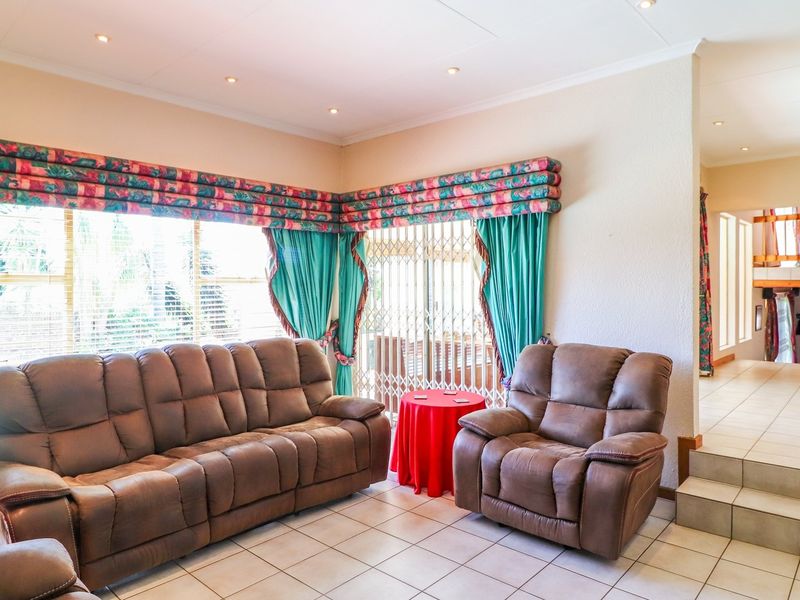 A spacious living room featuring tiled flooring, recessed lighting, and large windows with security gates, offering a bright and functional living space.