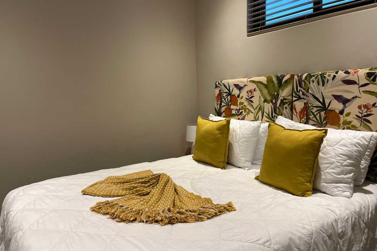 A cozy bedroom featuring neutral wall tones, a horizontal window with fitted blinds, and a decorative upholstered headboard.