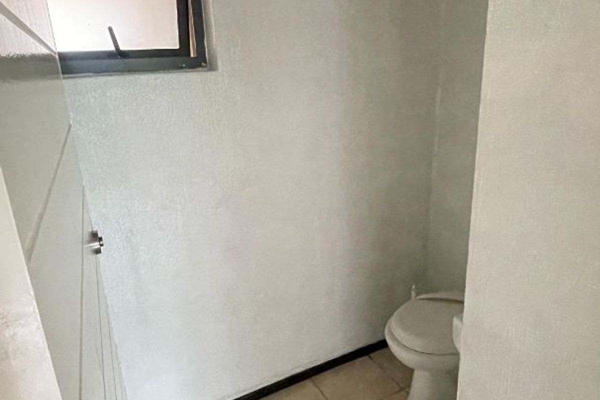 A compact bathroom featuring tiled flooring, a standard toilet, and a small window, offering a functional space in need of cosmetic updates.