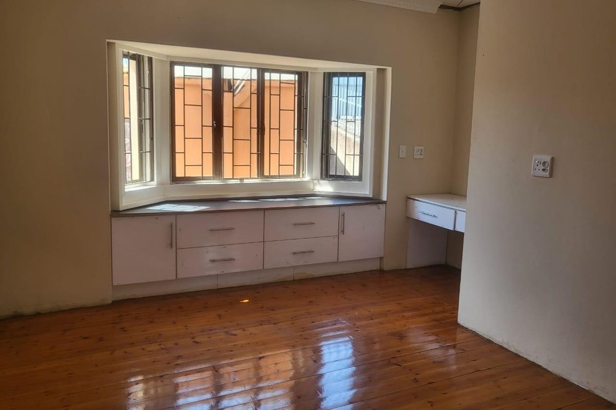 Empty bedroom featuring polished hardwood floors, a large bay window with integrated storage cabinetry, and a built-in desk area.