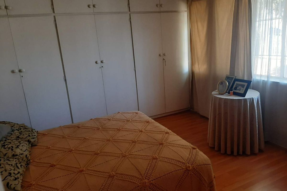 A bedroom featuring extensive built-in cupboards for storage and laminate flooring, offering a functional and neutral space.
