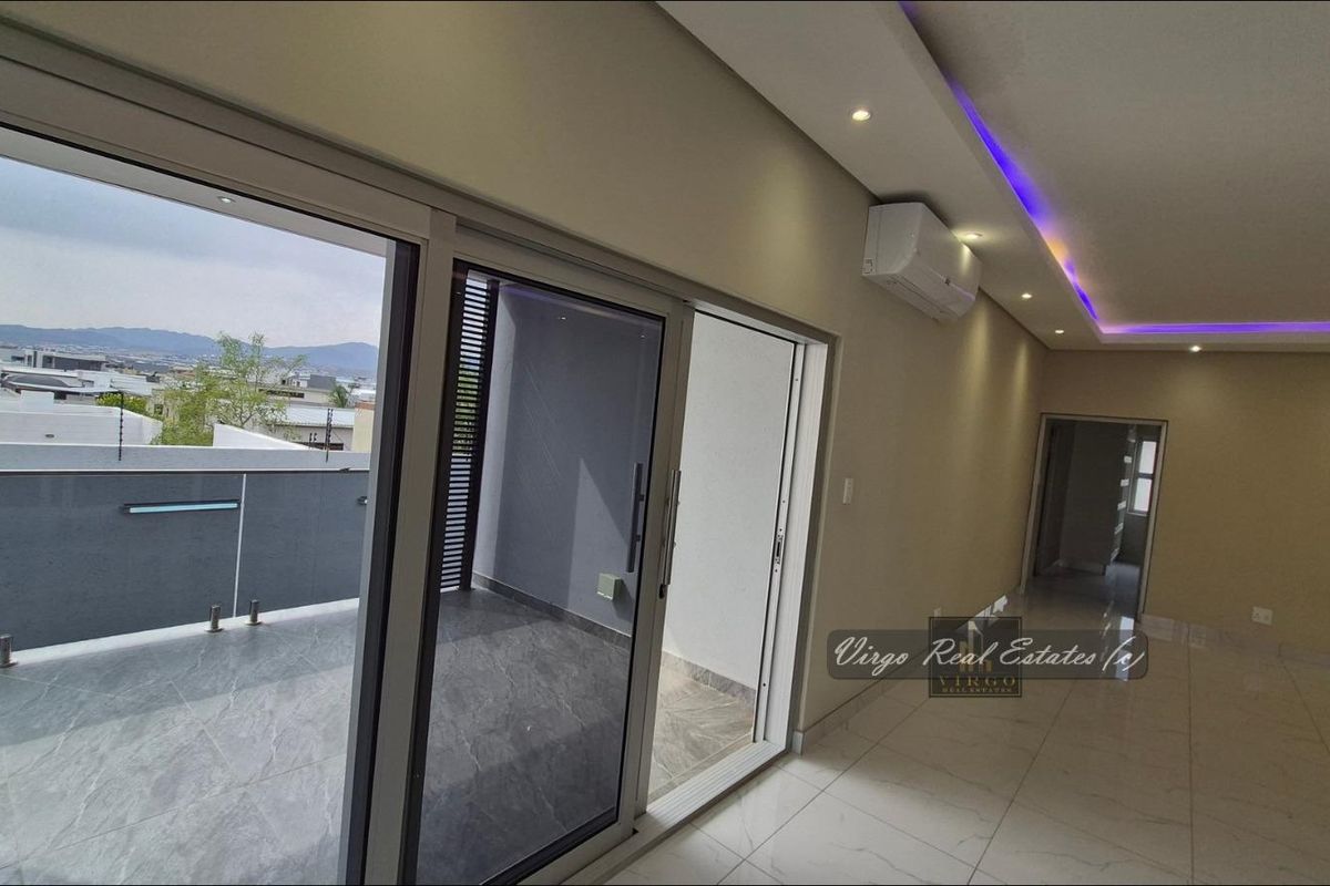 Spacious open-plan living area featuring modern tiled floors, recessed ceiling lighting with LED accents, and large sliding doors opening to a private balcony.