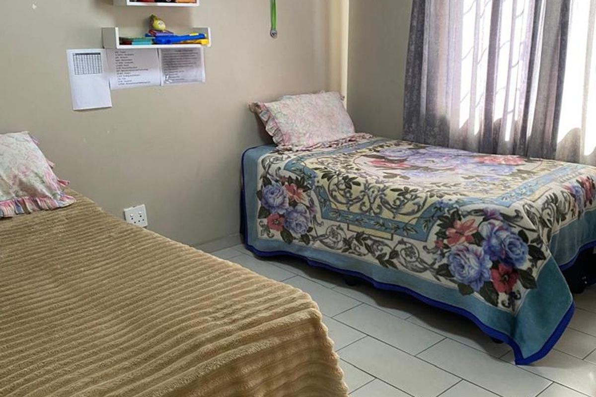A functional bedroom featuring tiled flooring and natural light through window curtains, providing a comfortable space for rest.