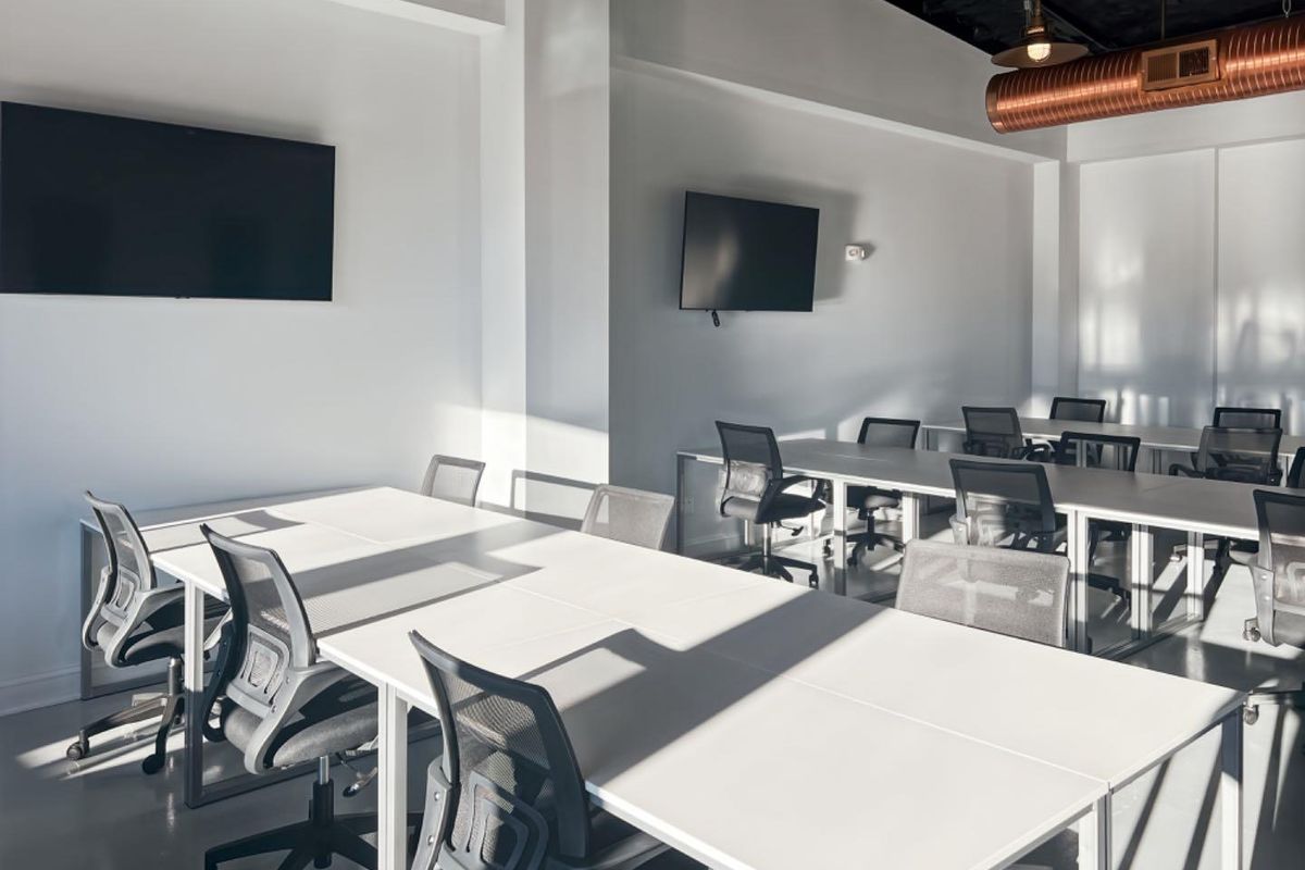 Modern open-plan office space featuring polished concrete floors, exposed industrial ductwork, and wall-mounted screens for collaborative work.