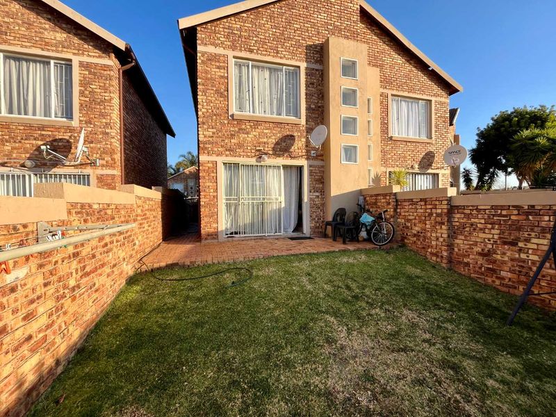 Rear view of a face brick townhouse featuring a private garden, paved patio area, and sliding door access to the interior living space.