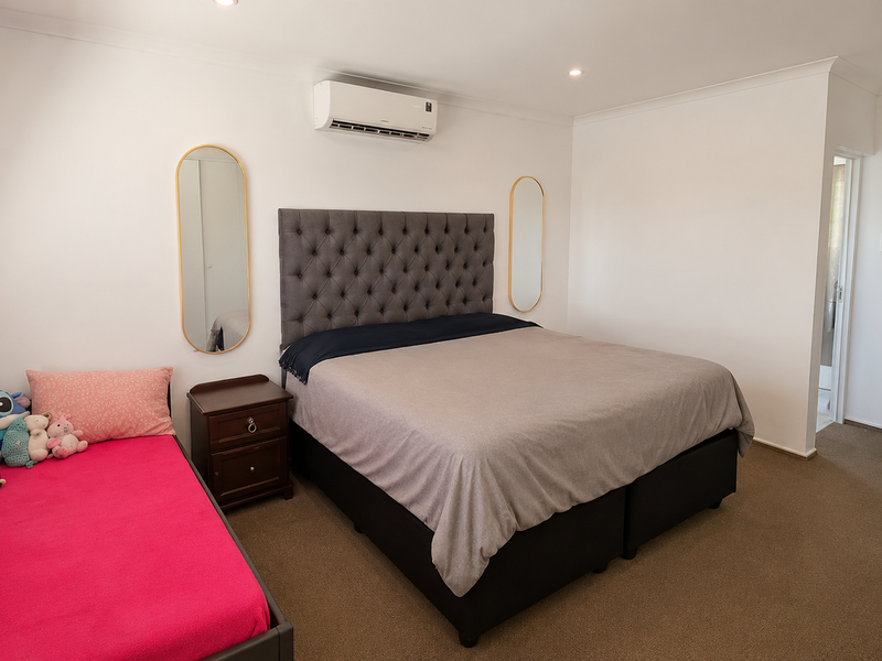 A well-maintained bedroom featuring neutral walls, carpet flooring, recessed downlighting, and a wall-mounted split-system air conditioning unit.