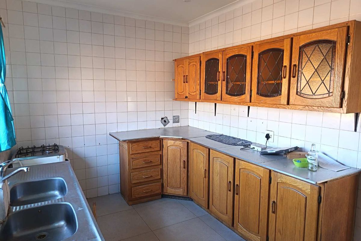 A functional kitchen featuring wooden cabinetry, a double stainless steel sink, gas hob, and tiled splashbacks, offering potential for a modern renovation.