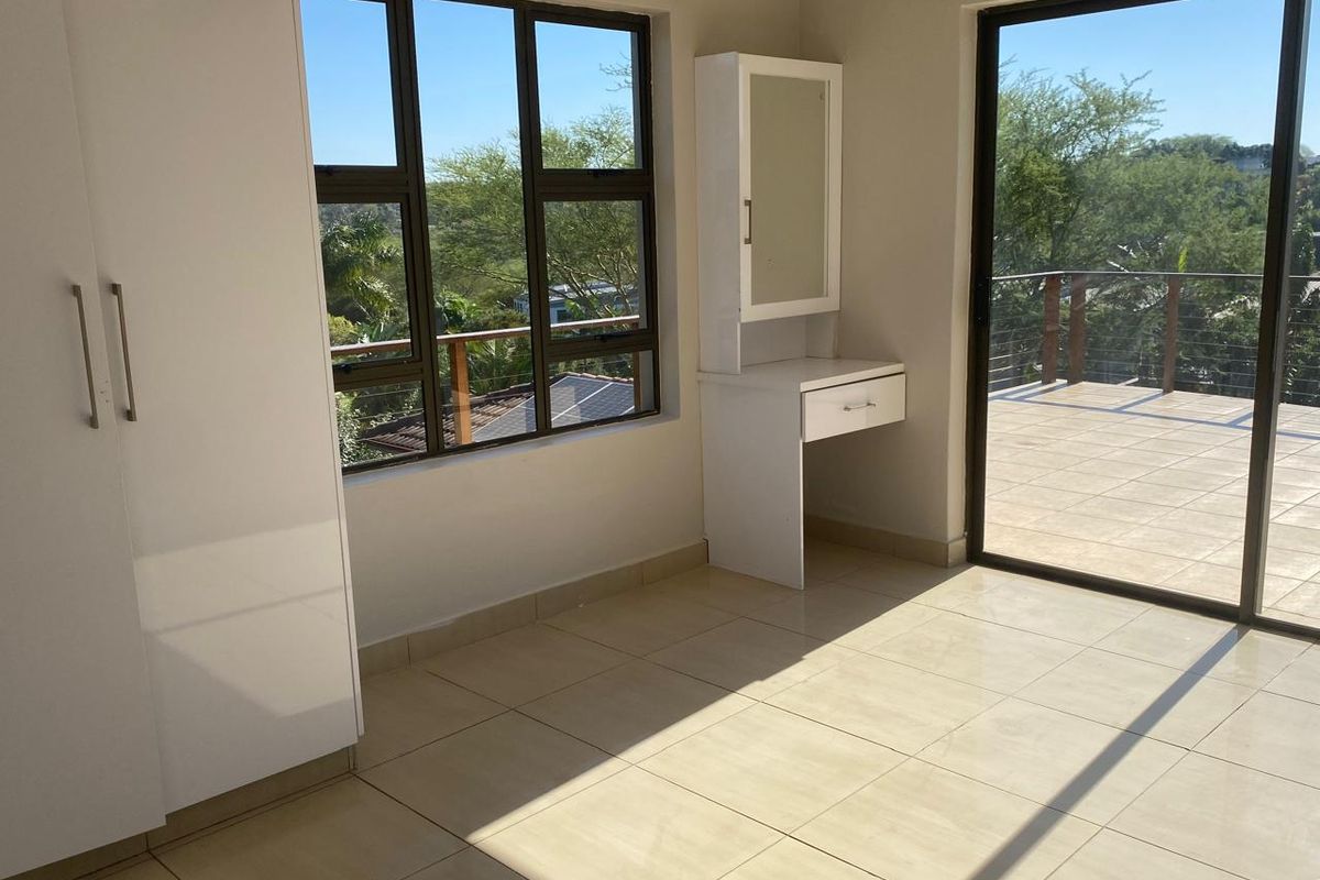 Bright bedroom featuring built-in cabinetry, tiled flooring, and direct access to a spacious outdoor balcony with scenic views.