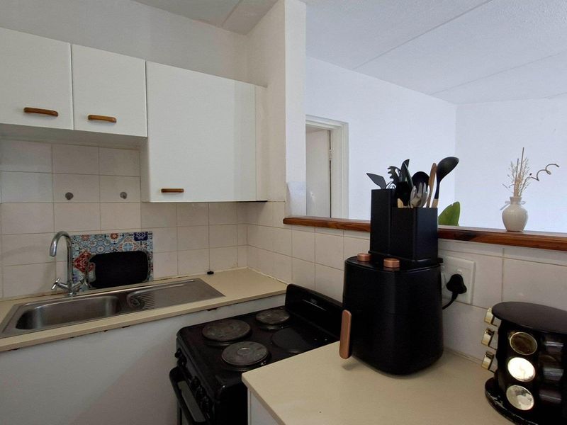 A compact kitchen featuring white cabinetry, a tiled backsplash, a stainless steel sink, and a freestanding electric stove with a laminate countertop.
