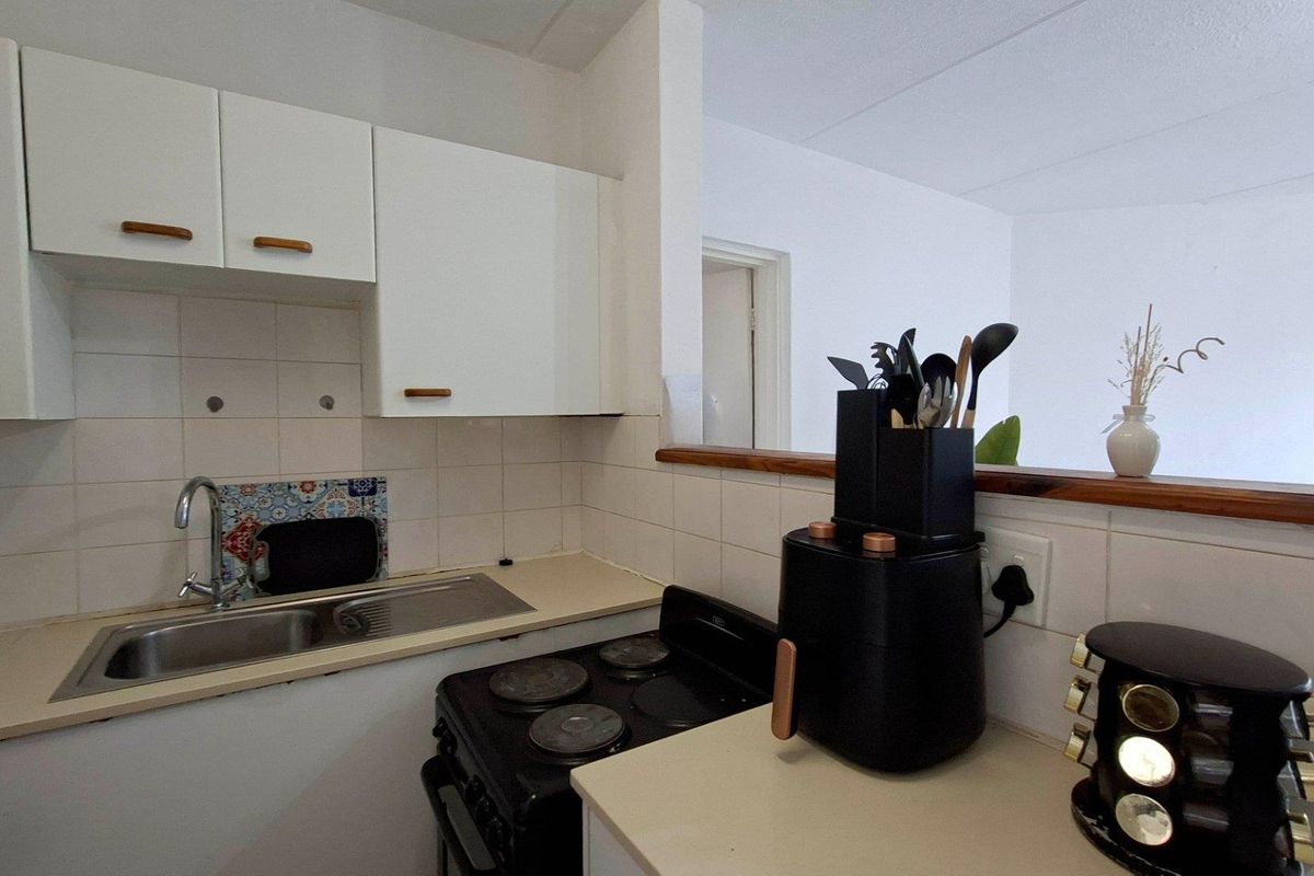 A compact kitchen featuring white cabinetry, a tiled backsplash, a stainless steel sink, and a freestanding electric stove with a laminate countertop.