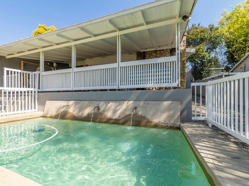 Outdoor pool area featuring a built-in water feature, concrete surround, and an adjacent covered patio with white railing.