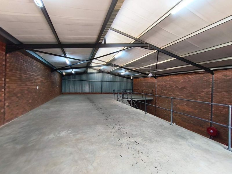 Spacious industrial mezzanine level featuring exposed brick walls, concrete flooring, and steel roof trusses, suitable for storage or workshop use.