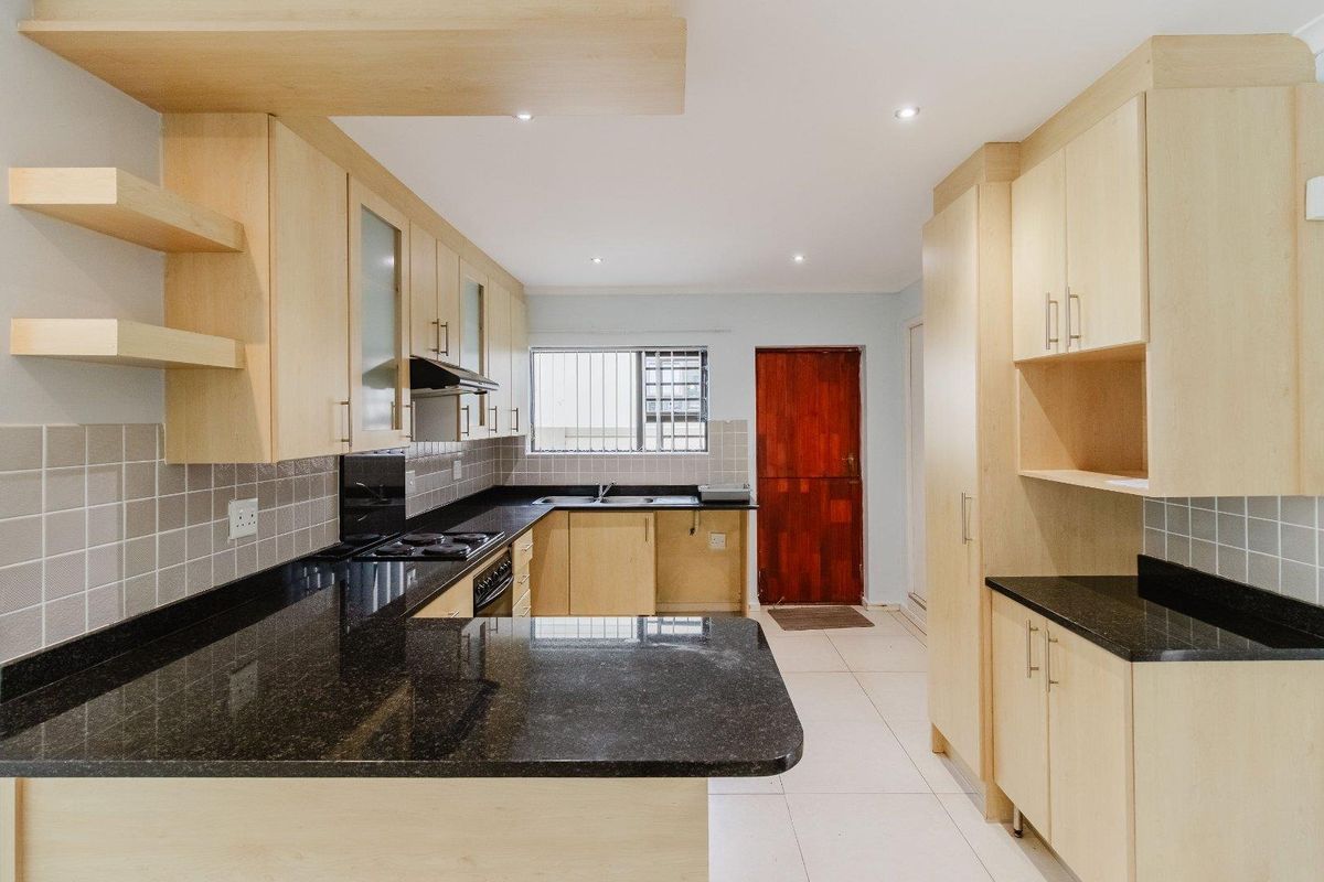 Modern kitchen featuring light wood cabinetry, contrasting black granite countertops, built-in stove with extractor fan, and tiled flooring.